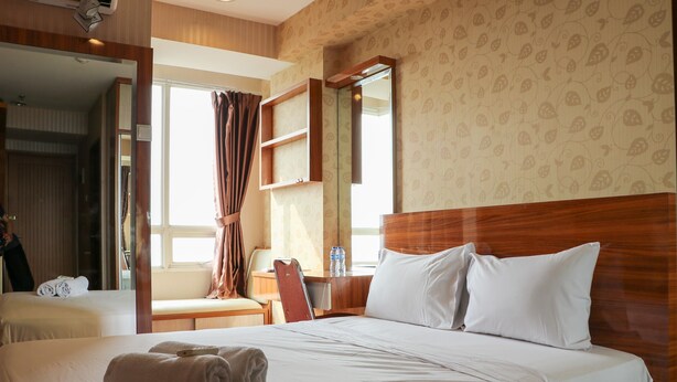 Une chambre d’hôtel avec deux lits, une tête de lit en bois, un grand miroir et une fenêtre avec des rideaux.
