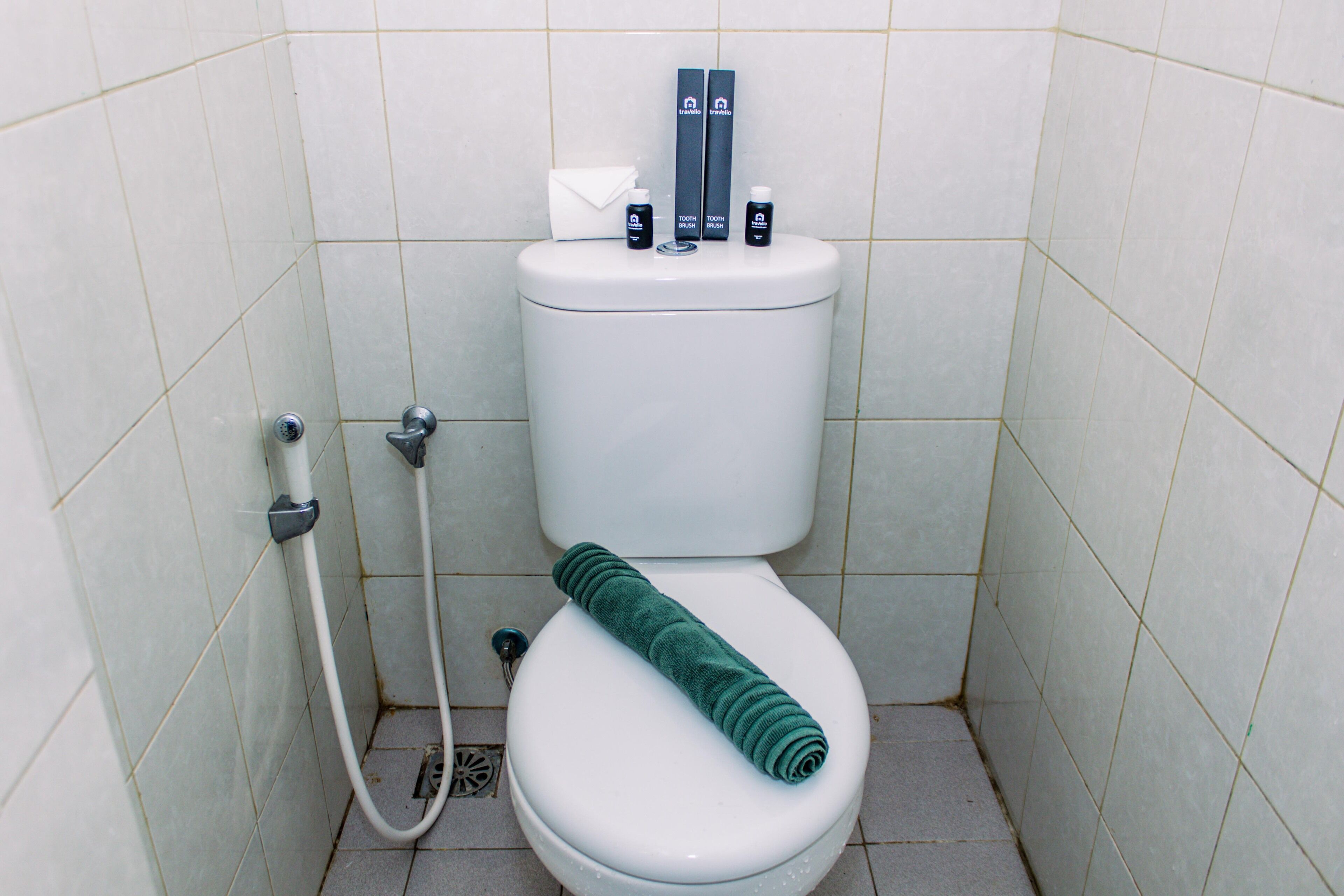 A bathroom with a toilet, a towel, and toiletries on the tank.