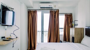 A hotel room with a bed, a TV mounted on the wall, and a balcony with curtains. - Comfort Stay Studio Room At Poris 88 Apartment (Tangerang)