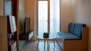 A compact hotel room with a sofa, a small table, a television, and a vending machine. - Nice And Homey 2Br Apartment At Capitol Park Residence (Jakarta)