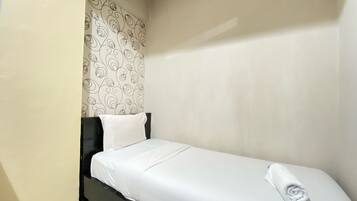 Une petite chambre avec un lit simple, un mur blanc uni et un papier peint à motifs sur un des murs.