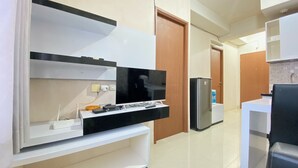 A modern kitchen with a built-in TV, a refrigerator, and a dining area with a white table and black chairs. - Cozy 2Br Apartment At Pinewood Jatinangor (Cileunyi)