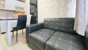 A modern living room with a black leather sofa and a dining area with a white countertop and a microwave. - Cozy 2Br Apartment At Pinewood Jatinangor (Cileunyi)