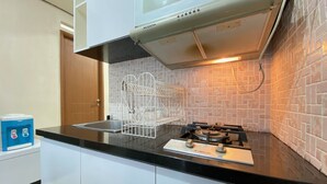 A kitchen with white cabinets, a black countertop, a gas stove, and a white wire rack. - Cozy 2Br Apartment At Pinewood Jatinangor (Cileunyi)