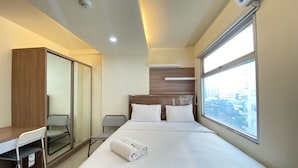Een hotelkamer met een bed, een bureau, een stoel, een kledingkast en een groot raam met uitzicht over de stad.