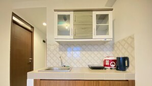 A kitchen with a wooden cabinet, a stainless steel sink, and a microwave on the countertop. - Gorgeous 2Br Apartment At Mekarwangi Square Cibaduyut (Bandung)