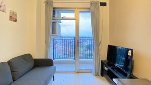 A living room with a sofa, a TV on a stand, and a balcony with a view of the city. - Gorgeous 2Br Apartment At Mekarwangi Square Cibaduyut (Bandung)