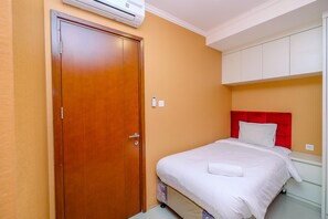 A hotel room with a wooden door, a bed with a red headboard, and white walls. - Comfort And Cozy 2Br At Signature Park Grande Apartment (Jakarta)