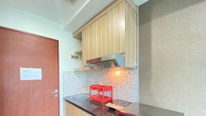 A compact kitchen with wooden cabinets, a stainless steel sink, a red appliance, and a tiled backsplash. - Comfy Studio Apartment At Taman Melati Jatinangor (Hegarmanah)