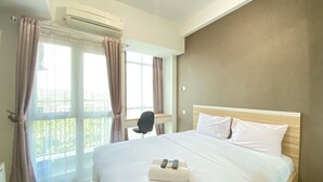 A hotel room with a large bed, a desk, and a window with curtains. - Comfy Studio Apartment At Taman Melati Jatinangor (Hegarmanah)