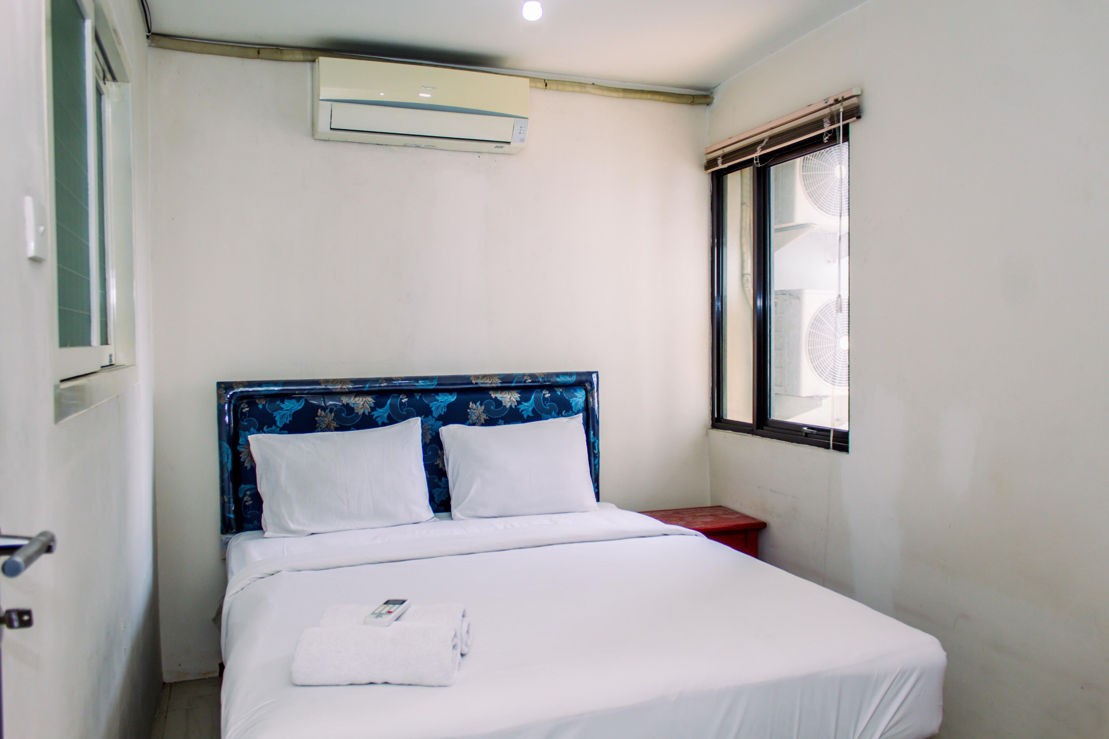 Uma cama de solteiro com cabeceira floral, roupa de cama branca e uma janela com vista para o exterior.