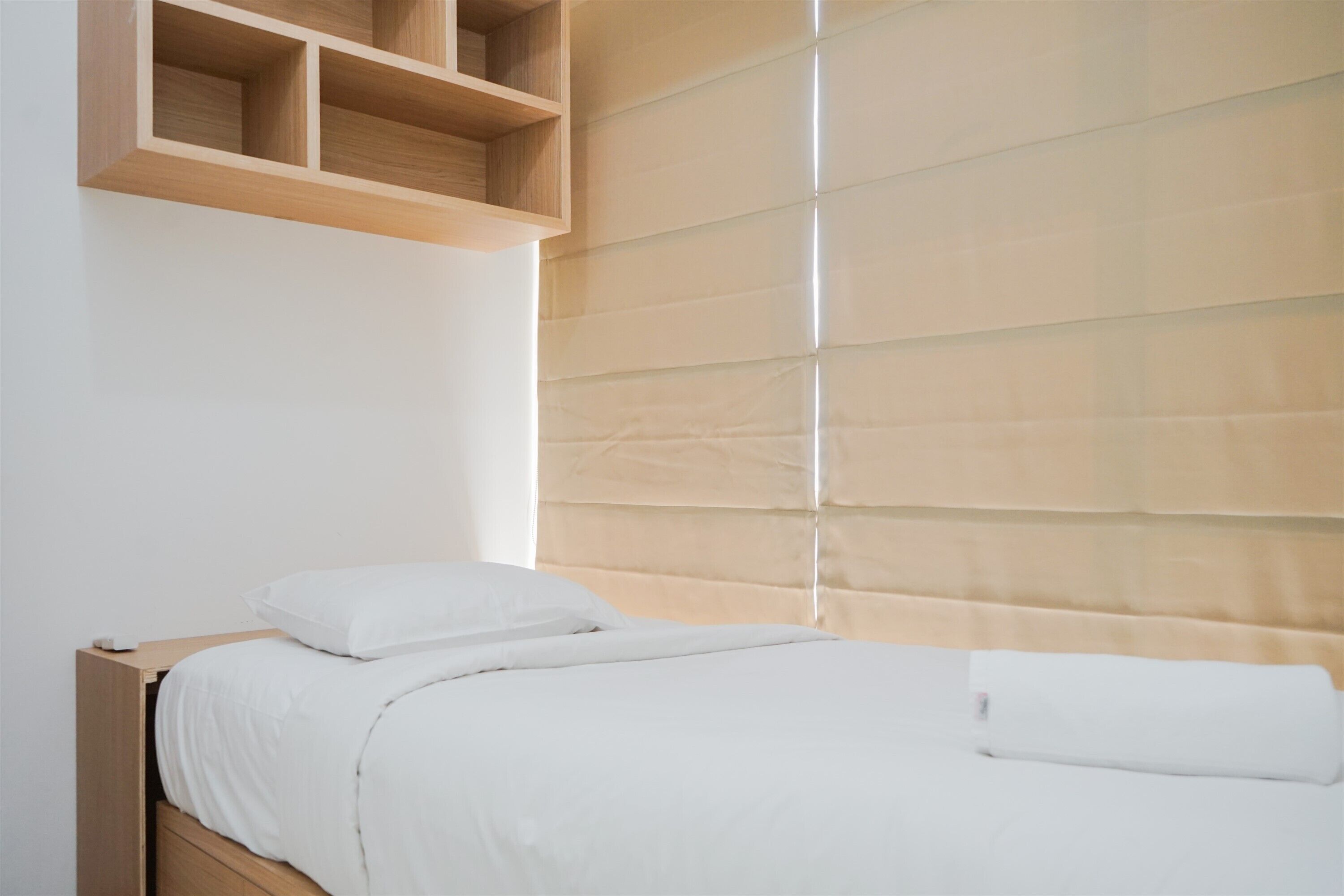 Ein ordentlich bezogenes Bett mit weißer Bettwäsche, einem Holz-Kopfteil und einem eingebauten Regal darüber.
