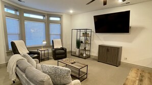 A modern living room with a sofa, armchairs, a coffee table, a TV, and a ceiling fan. - BRAND NEW The Townie (Cedar City)