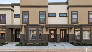 A row of townhouses with a uniform architectural style, featuring bay windows and a central entrance with a door and a wreath. - BRAND NEW The Townie (Cedar City)