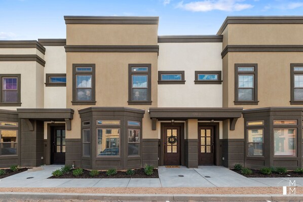 A row of townhouses with a uniform architectural style, featuring bay windows and a central entrance with a door and a wreath.