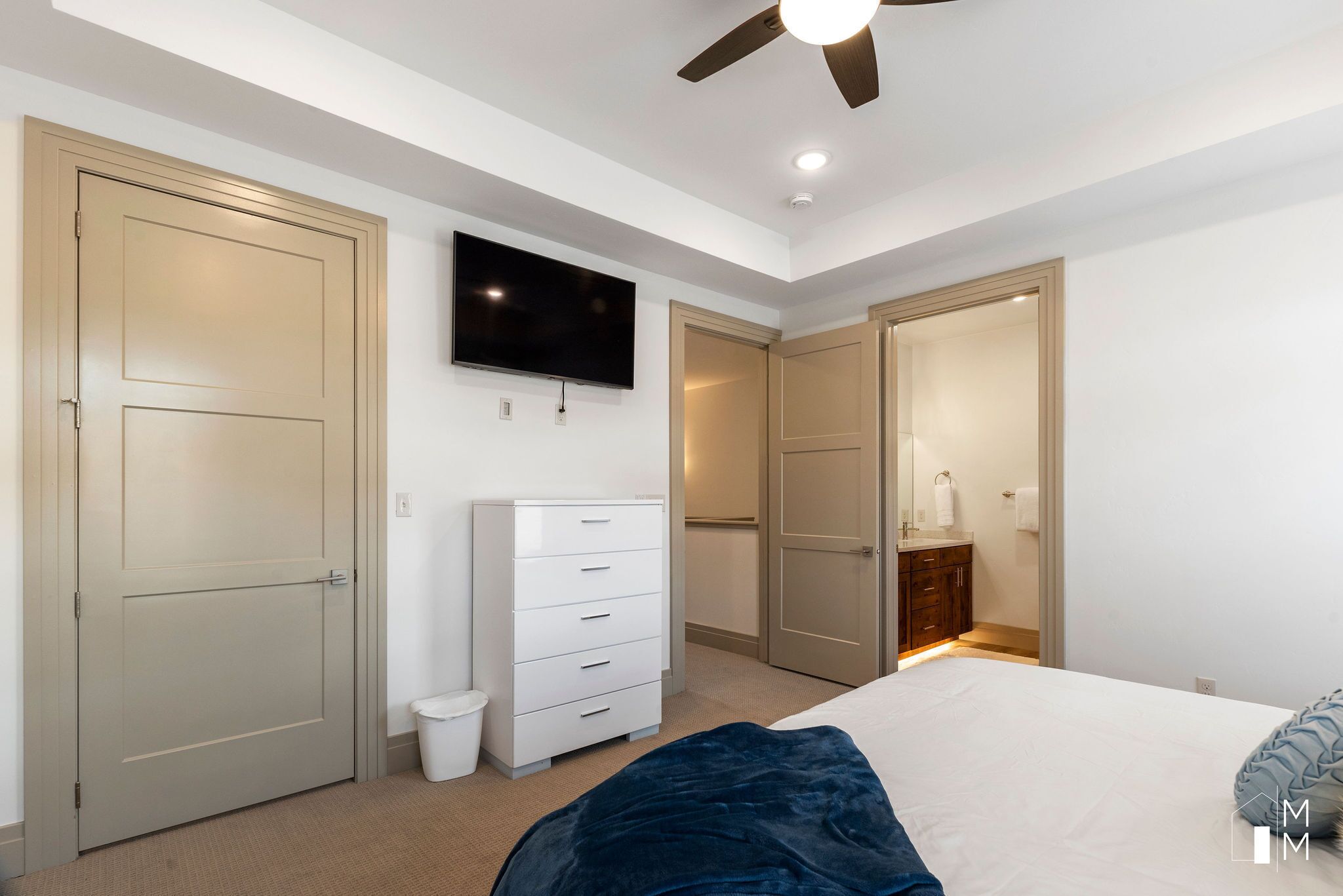 A bedroom with a bed, a dresser, a television, and a ceiling fan.