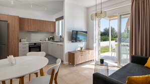 A modern kitchen with wooden cabinets, a dining area with a white table and chairs, and a living area with a sofa and a TV. - New Brand Villas,Heating Pool, Jacuzzi ,Spa near haraki beach,taverna,market (Charaki)