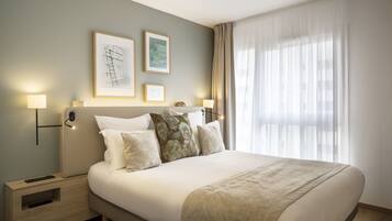 A hotel room with a large bed, two bedside tables, a headboard, and two wall-mounted lamps.