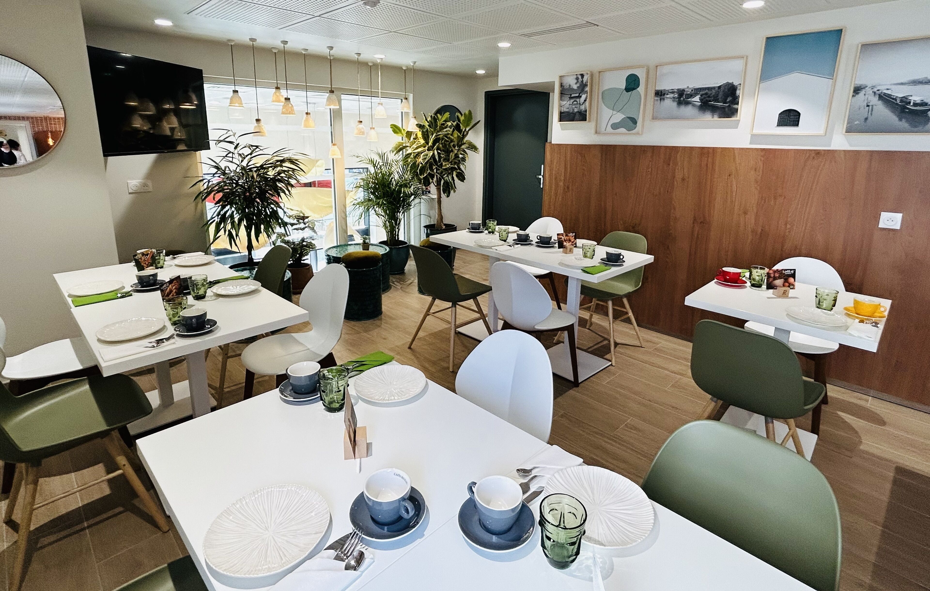 A modern dining area with white tables, green chairs, and potted plants.