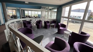 Ein modernes Interieur mit violetten Sitzgelegenheiten, großen Fenstern und Blick ins Freie.
