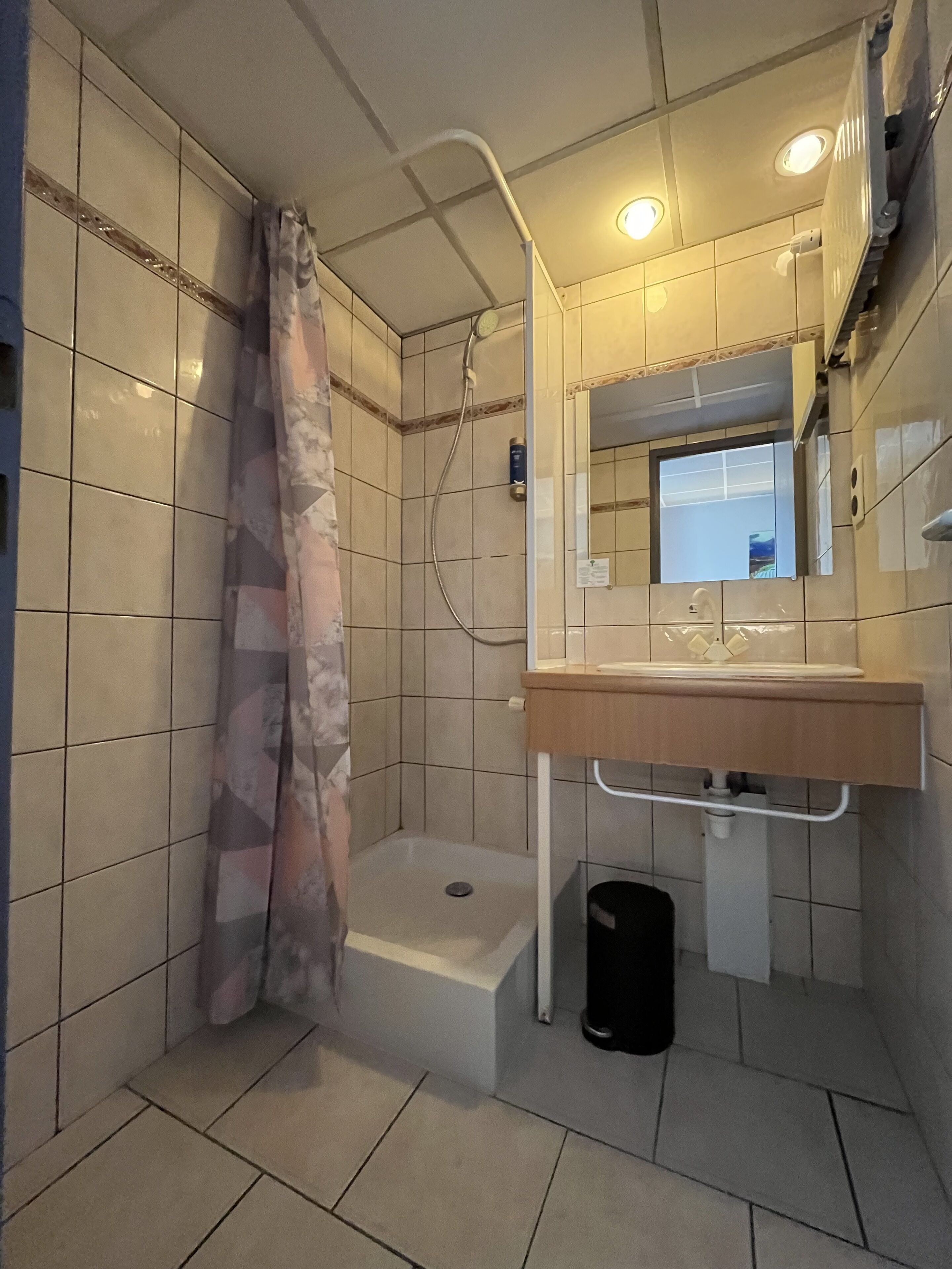 Ein Badezimmer mit Dusche, Waschbecken mit Spiegel und Fliesenwänden.