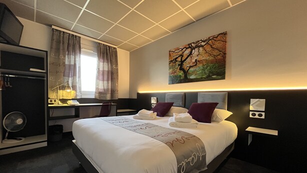 Ein Hotelzimmer mit einem großen Bett, einem Schreibtisch, einem Stuhl, einem Ventilator und einem Bild an der Wand.