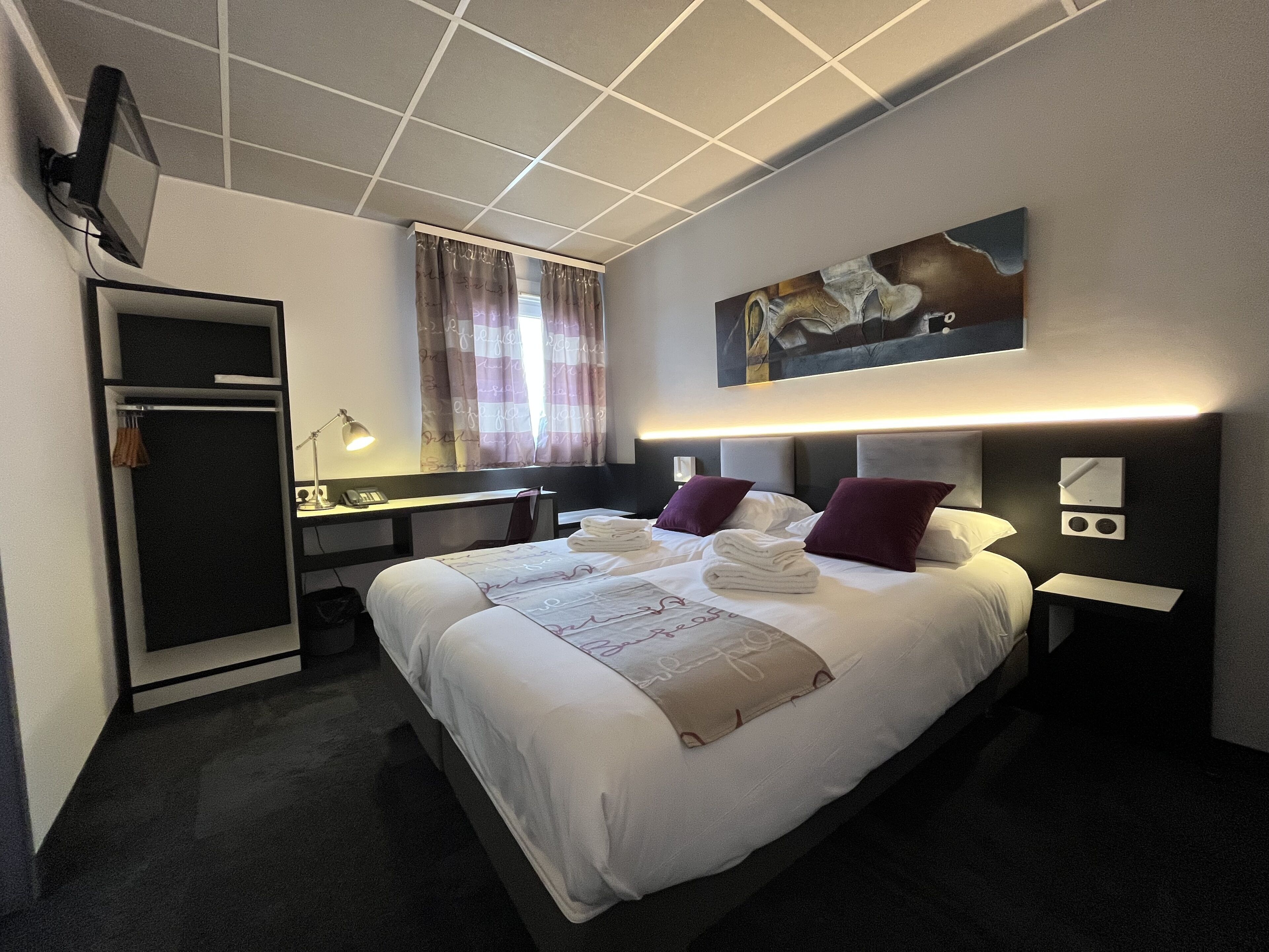 Een hotelkamer met een bed, een bureau, een stoel, een kledingkast en een televisie.