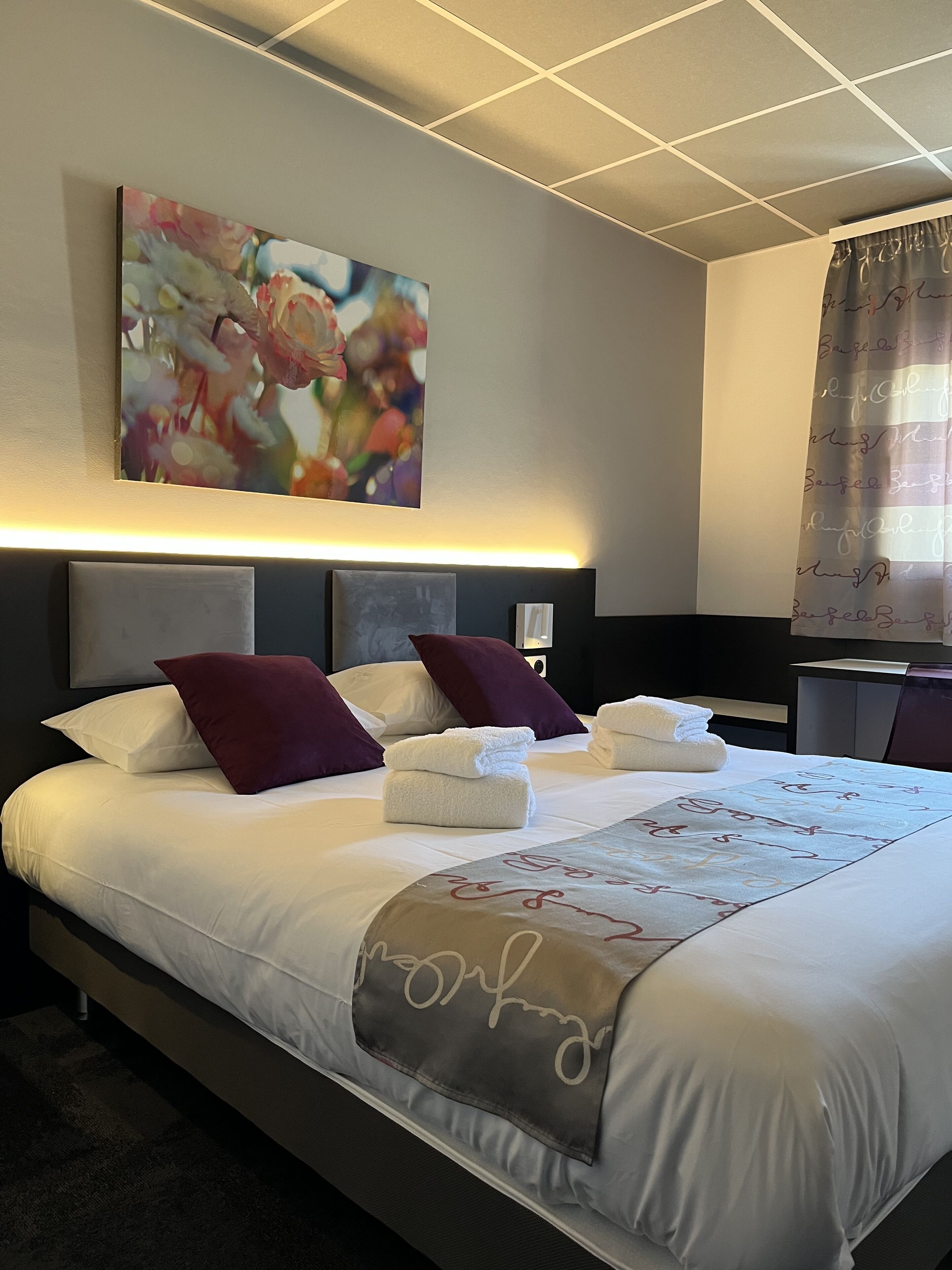 Habitación de hotel con una cama bien hecha, un cuadro grande sobre la cama y una mesita de noche con una lámpara.