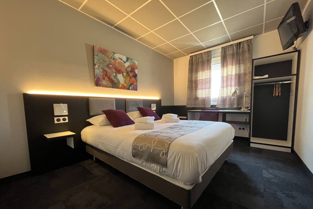 Ein modernes Hotelzimmer mit einem großen Bett, Nachttischen, einem Schreibtisch und einem Fernseher.