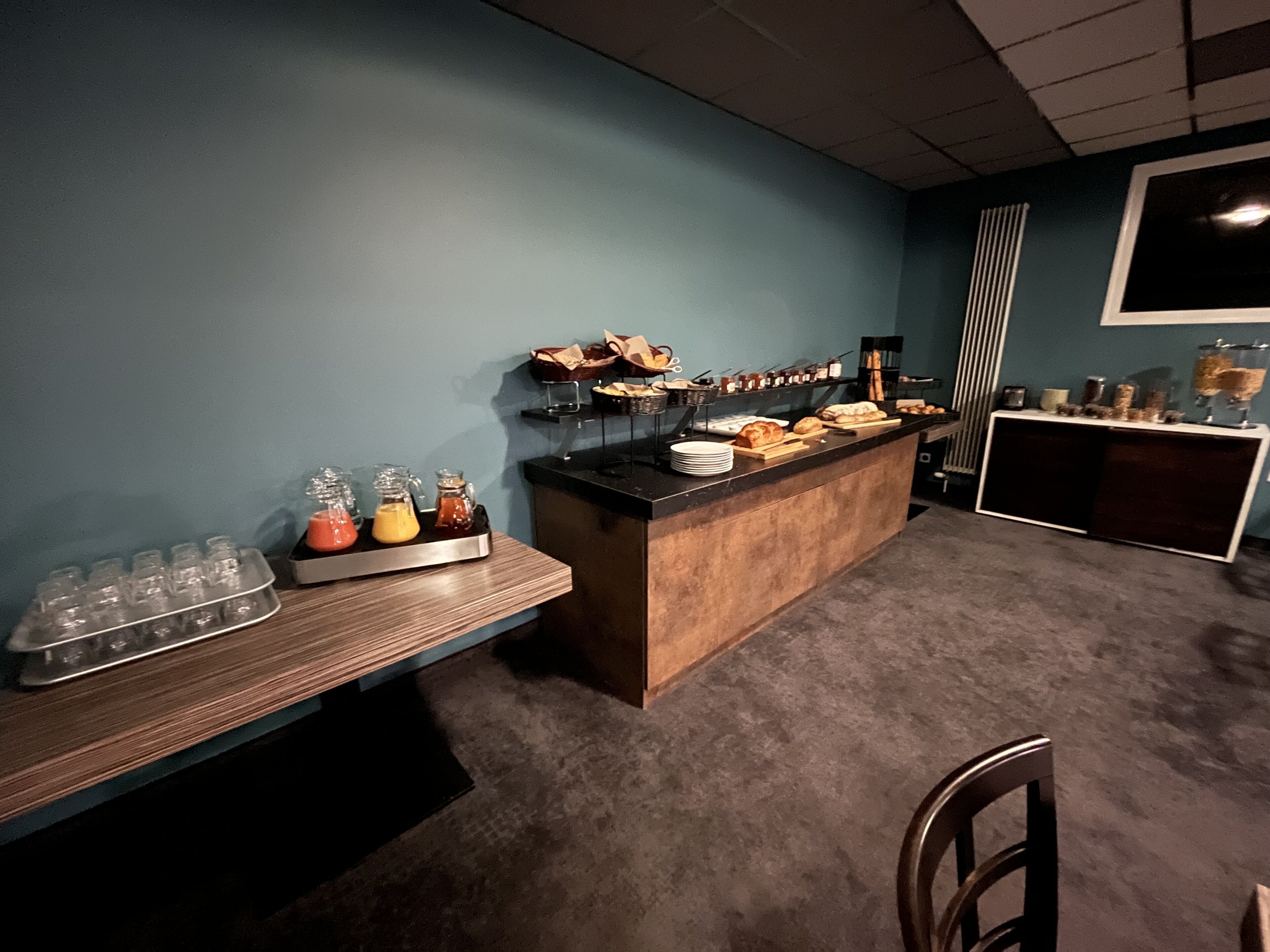 Un bar où l’on peut prendre le petit-déjeuner, proposant une variété de plats et de boissons, un espace avec des sièges et une grande fenêtre en arrière-plan.