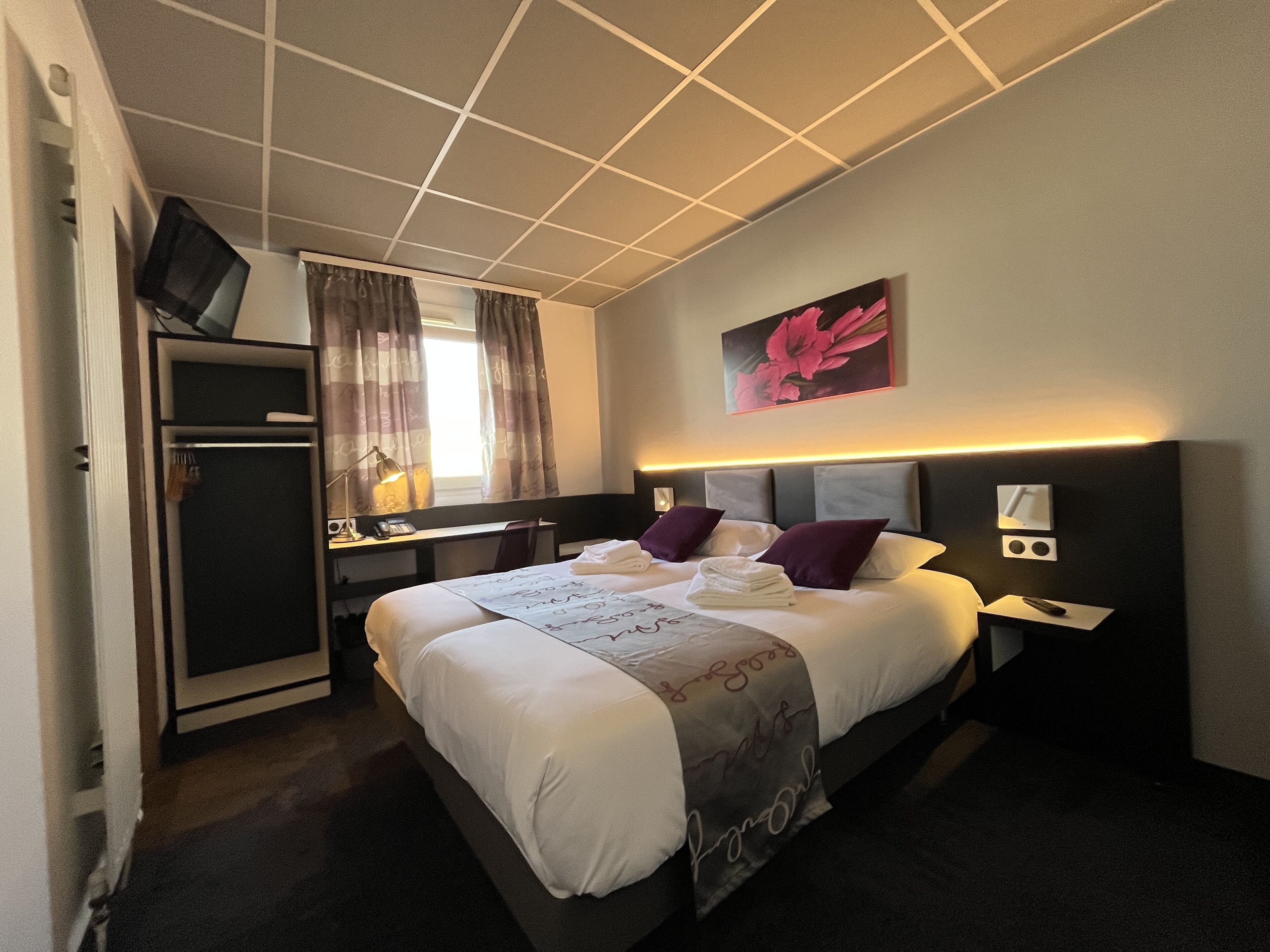Habitación de hotel con cama, mesitas de noche, escritorio, armario, televisor y un cuadro en la pared.
