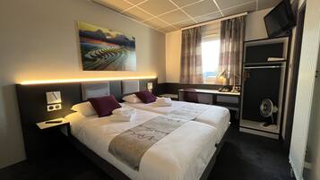 Een hotelkamer met een groot bed, een bureau, een stoel, een televisie en een raam met gordijnen.