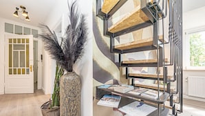 Een modern interieur met een houten trap, een decoratieve vaas met veertjes en een metalen plank met tijdschriften.