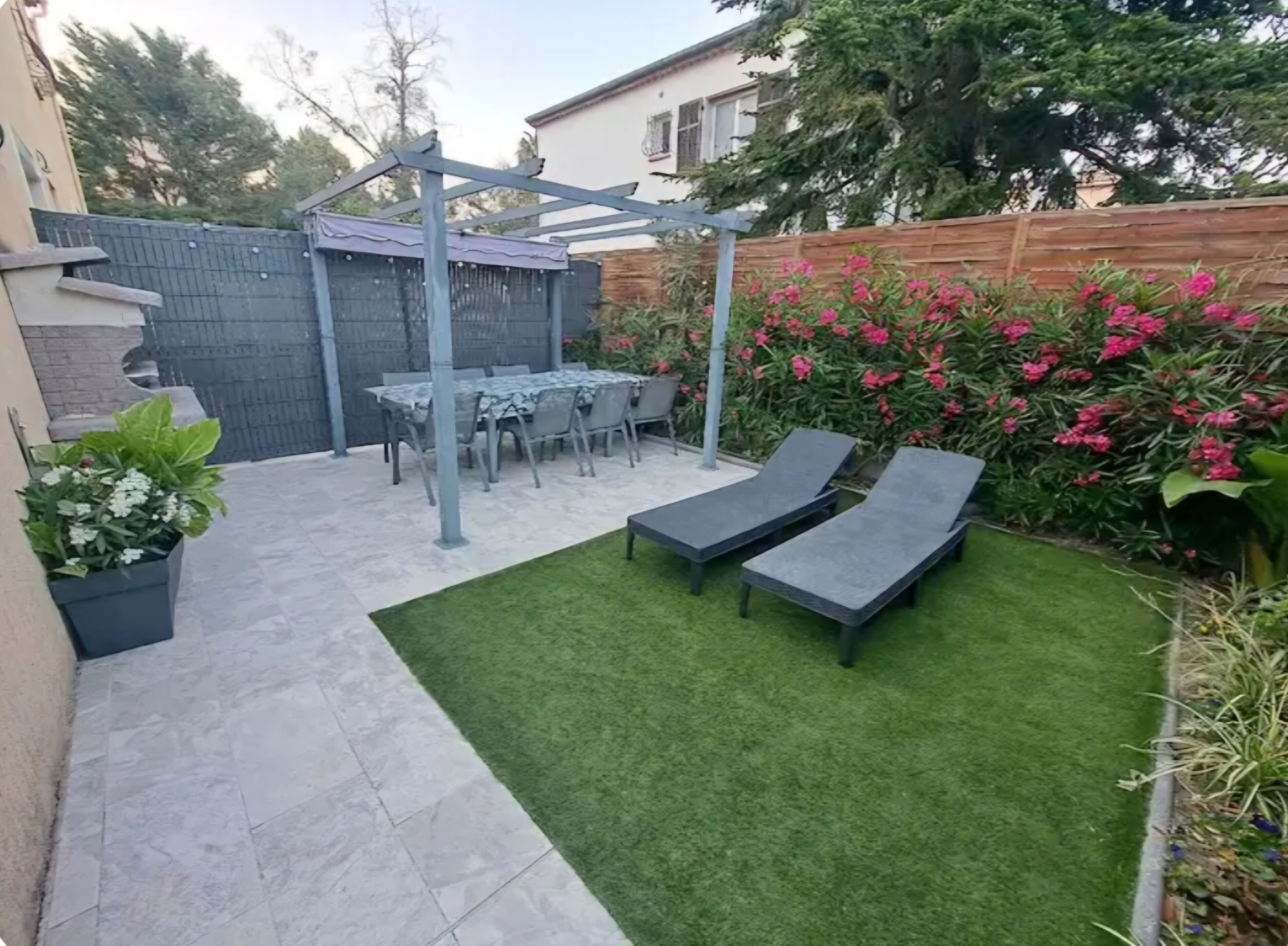 Uma área de pátio com mesa e cadeiras, uma pérgola e duas poltronas.