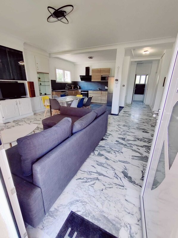 A modern living room with a grey sofa, a TV, and a kitchen in the background.