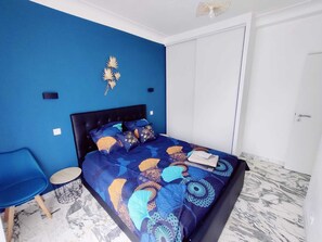 A bedroom with a blue wall, a bed with patterned bedding, a small round table, and a door.