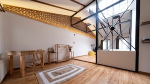 Une pièce spacieuse avec un plancher en bois, un coin repas comprenant une table et des chaises, une grande fenêtre offrant une belle vue et un mur décoratif en briques.