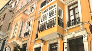 Un immeuble à plusieurs étages, doté d’une façade jaune, de grandes fenêtres et d’un balcon avec des balustrades noires.