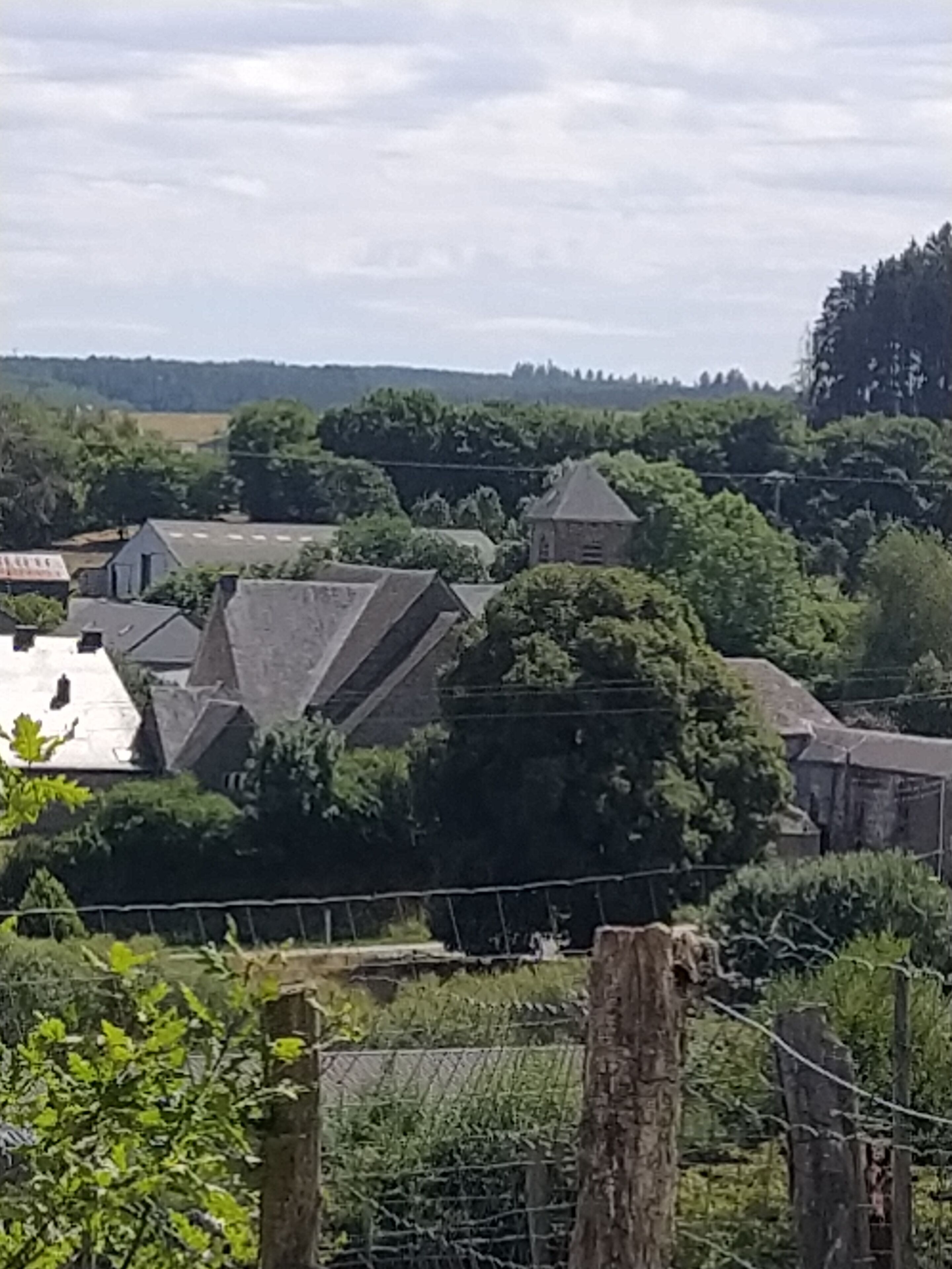 Un village rural aux maisons traditionnelles en pierre, entouré d’une végétation luxuriante et sous un ciel dégagé.