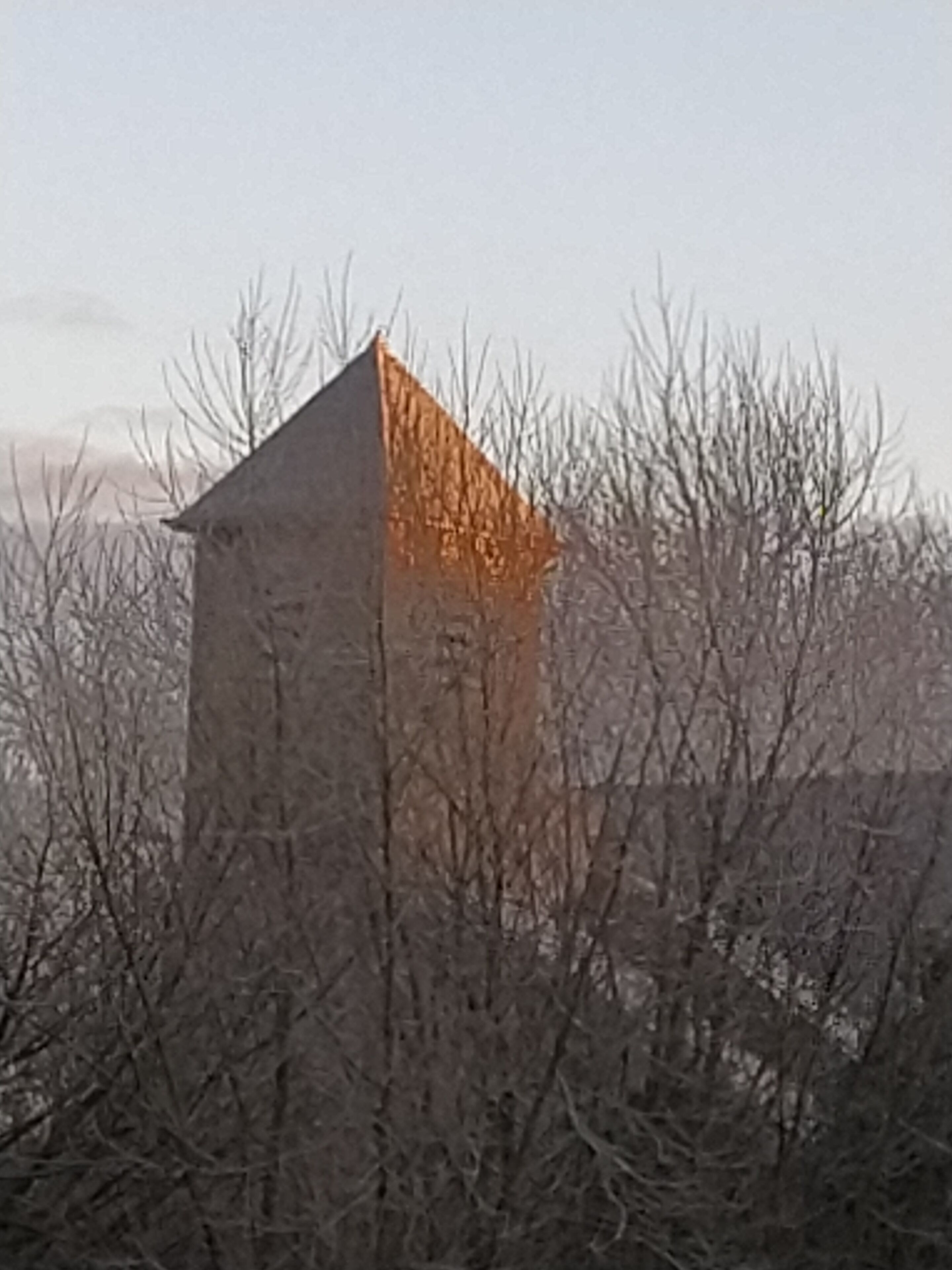 A stone building with a triangular roof, surrounded by leafless trees.