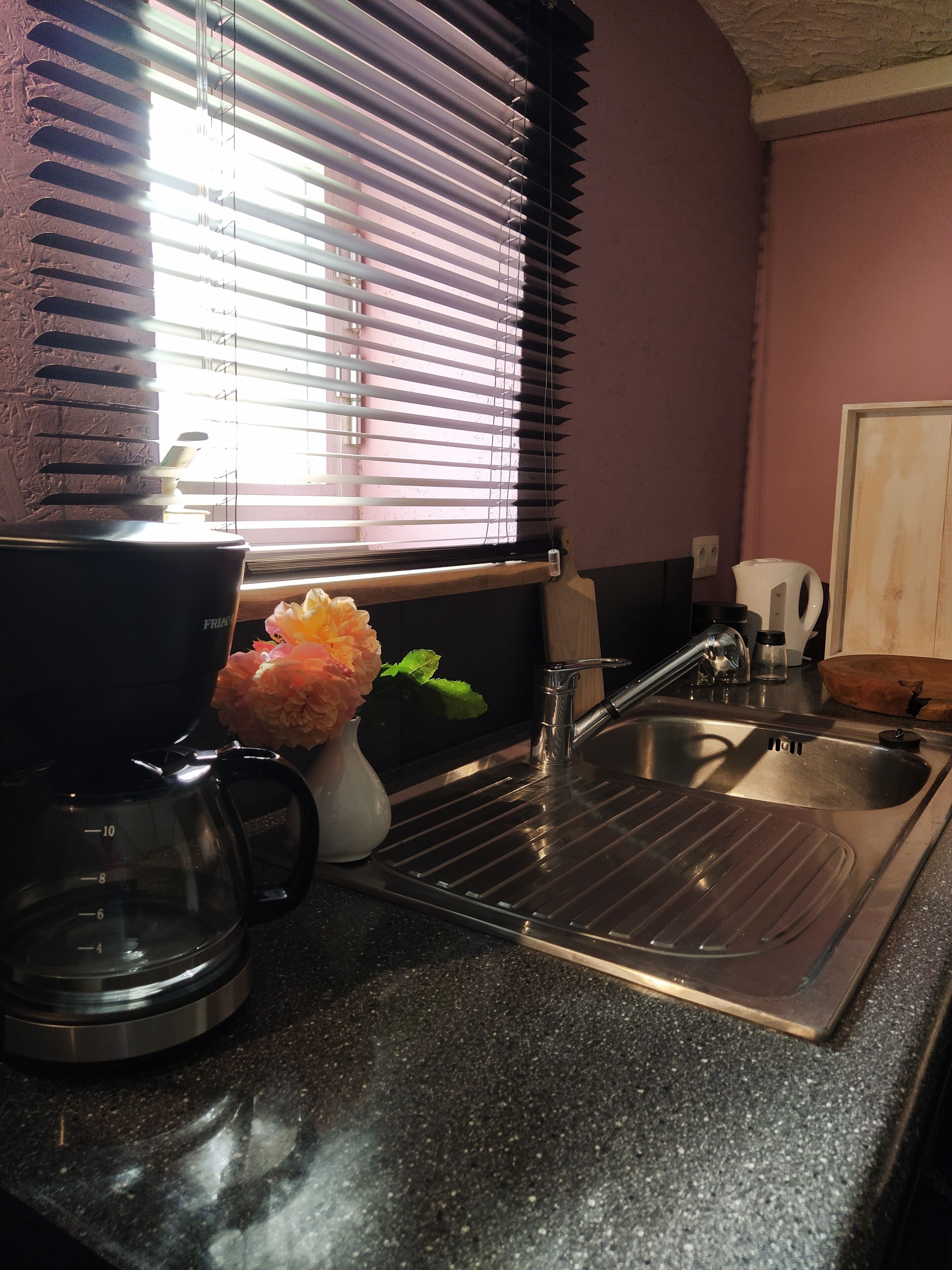 A kitchen with a coffee maker, a sink, and a window with blinds.