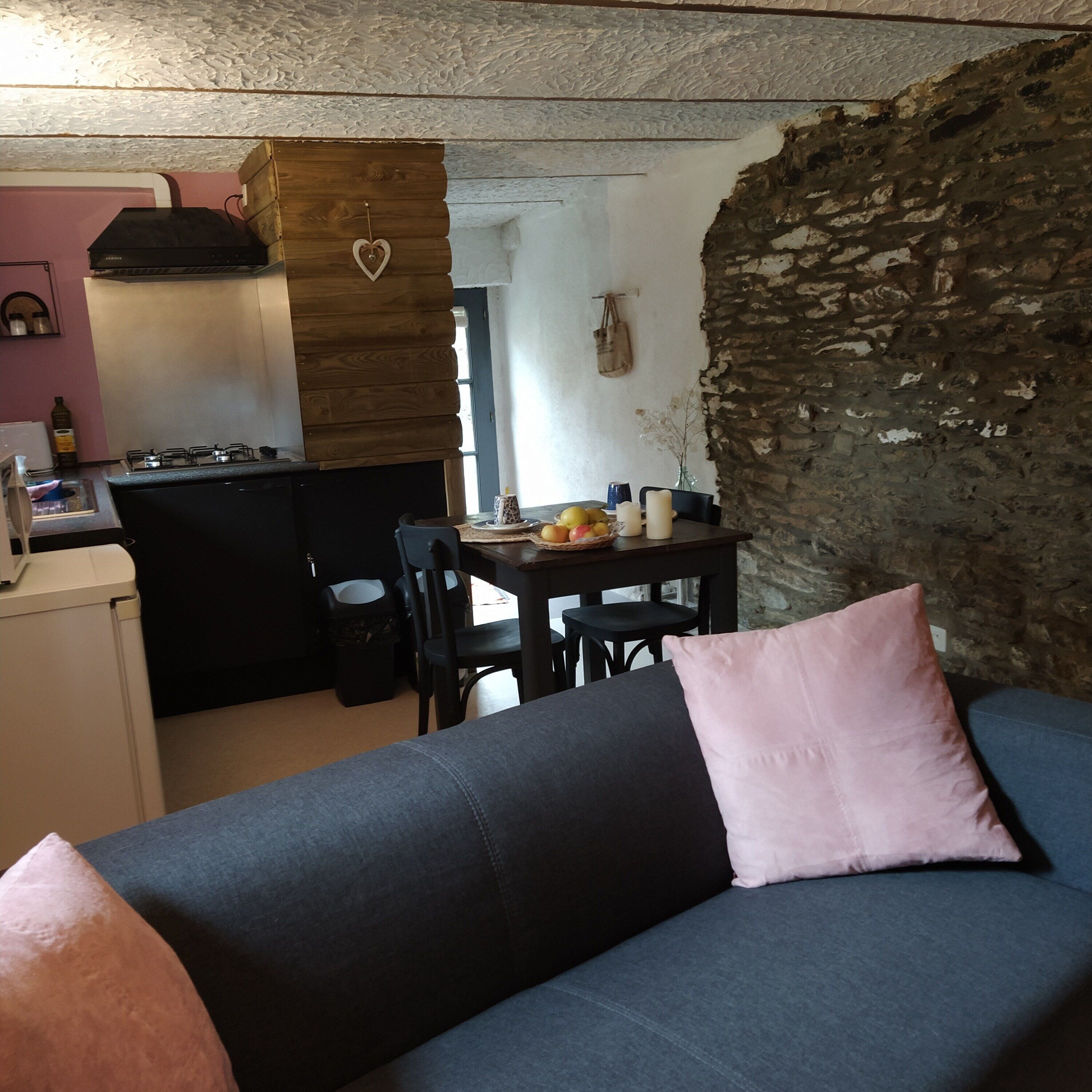 A cozy living space with a sofa, a dining table with fruit, a kitchen area, and a stone wall.