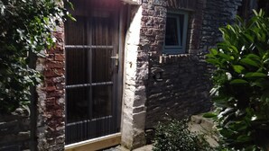 Un bâtiment en pierre avec une porte en métal, une petite fenêtre et un chemin de gravier menant à l’entrée.