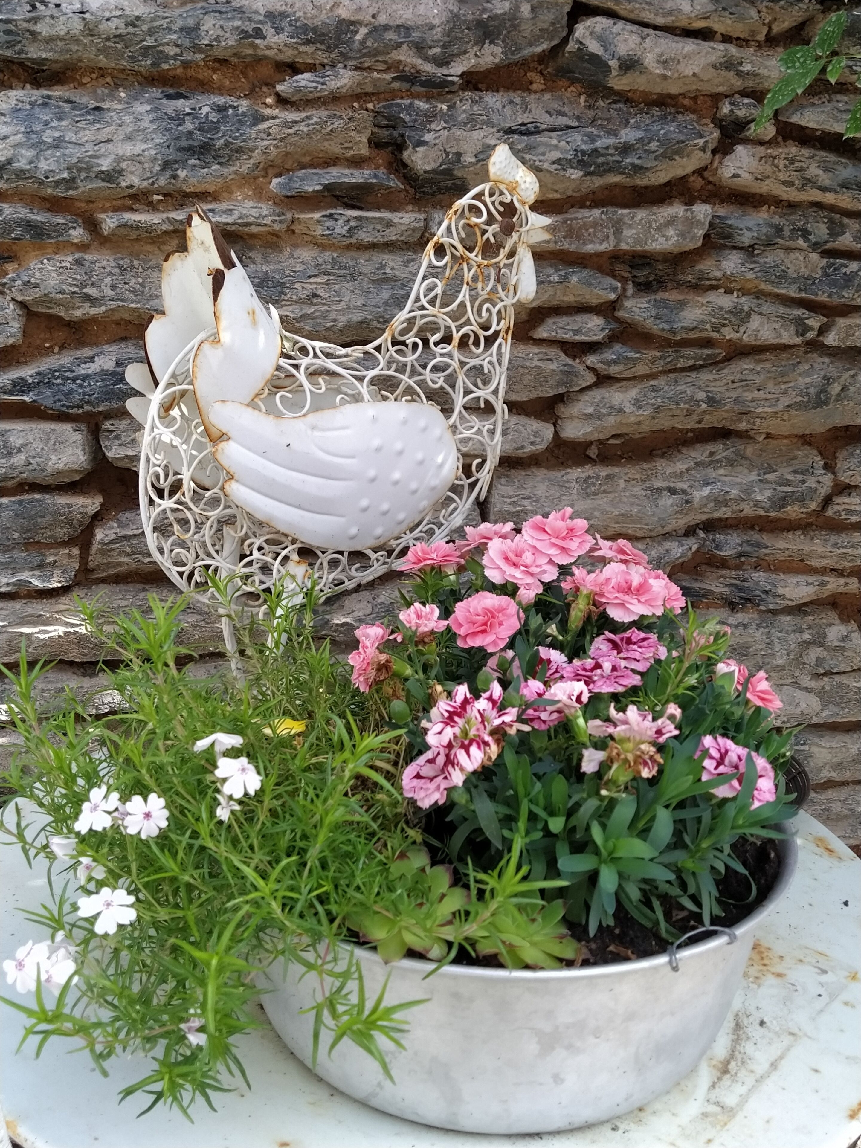 A planter with pink flowers and a decorative metal chicken sculpture.