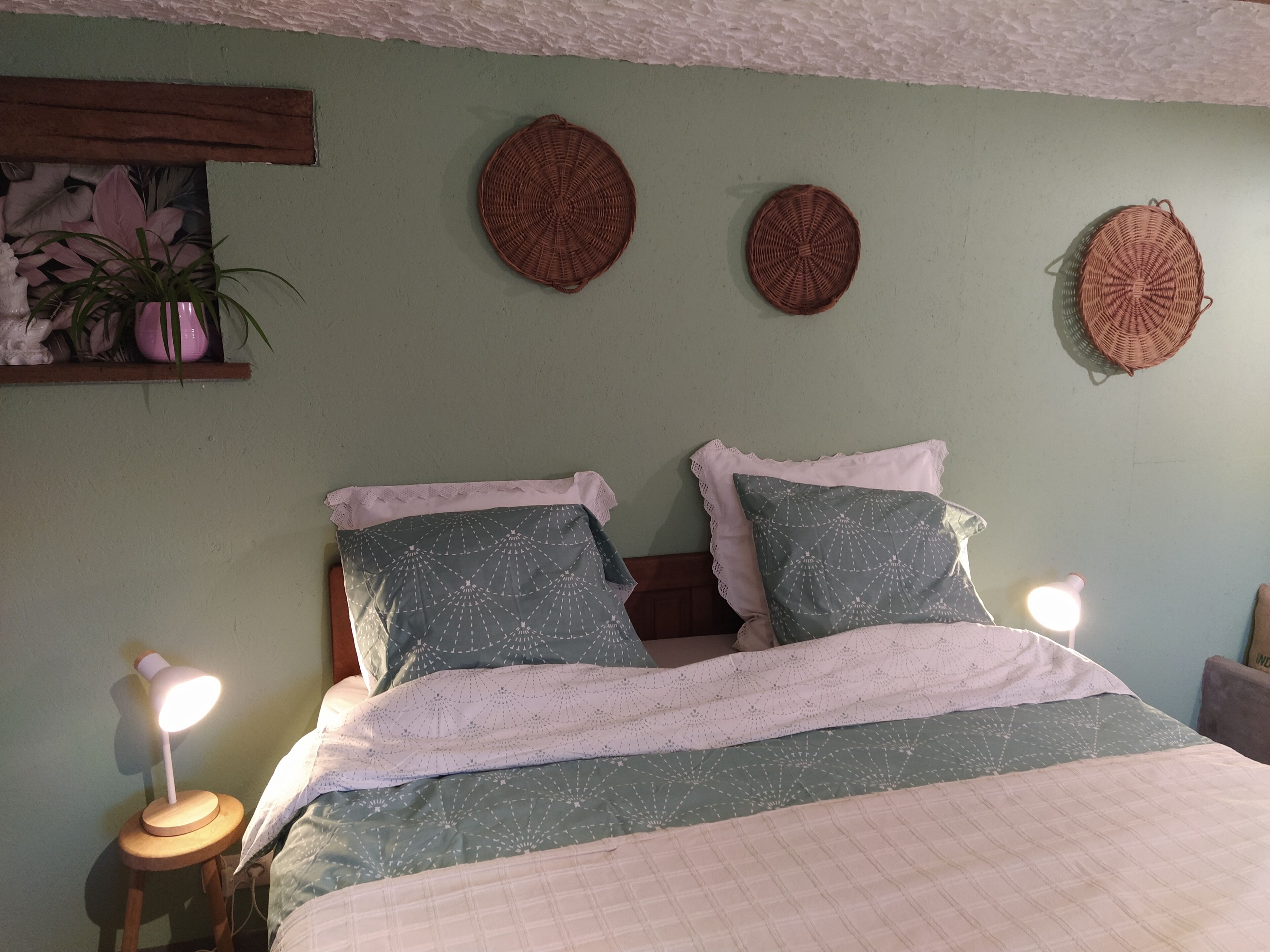 A bedroom with a bed, two bedside lamps, a shelf with decorative items, and wall-mounted woven baskets.