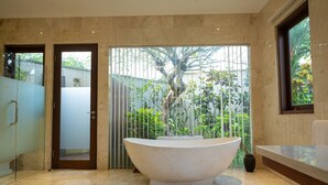 Een moderne badkamer met een vrijstaand bad, een douchecabine met glazen wanden en uitzicht op een weelderige tuin door een schuifdeur.