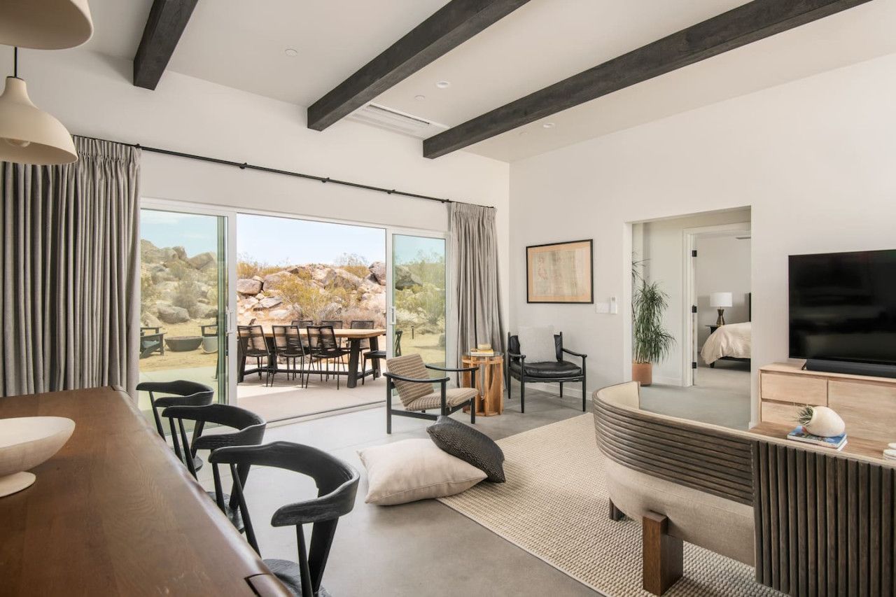 Uma sala de estar moderna com uma televisão grande, uma área de jantar com mesa e cadeiras, e vista para o exterior.