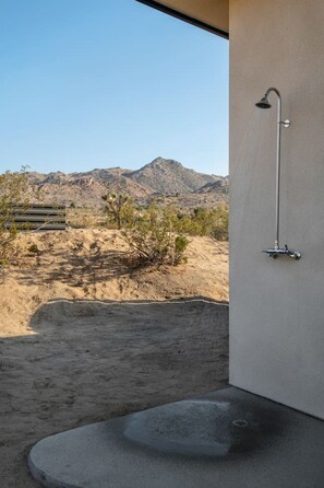 A modern bathroom with a shower, a concrete step leading to a patio, and a view of a desert landscape with mountains in the background.