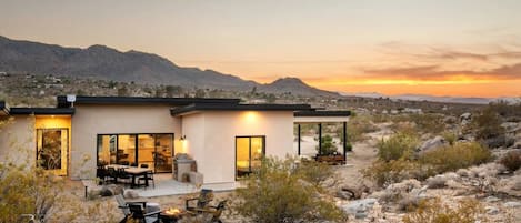 A modern house with a patio, outdoor seating, and a view of mountains at sunset.