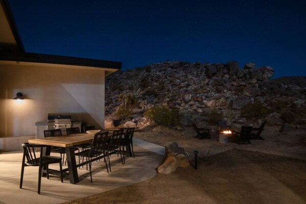 An outdoor patio with a dining table and chairs, a grill, and a fire pit.